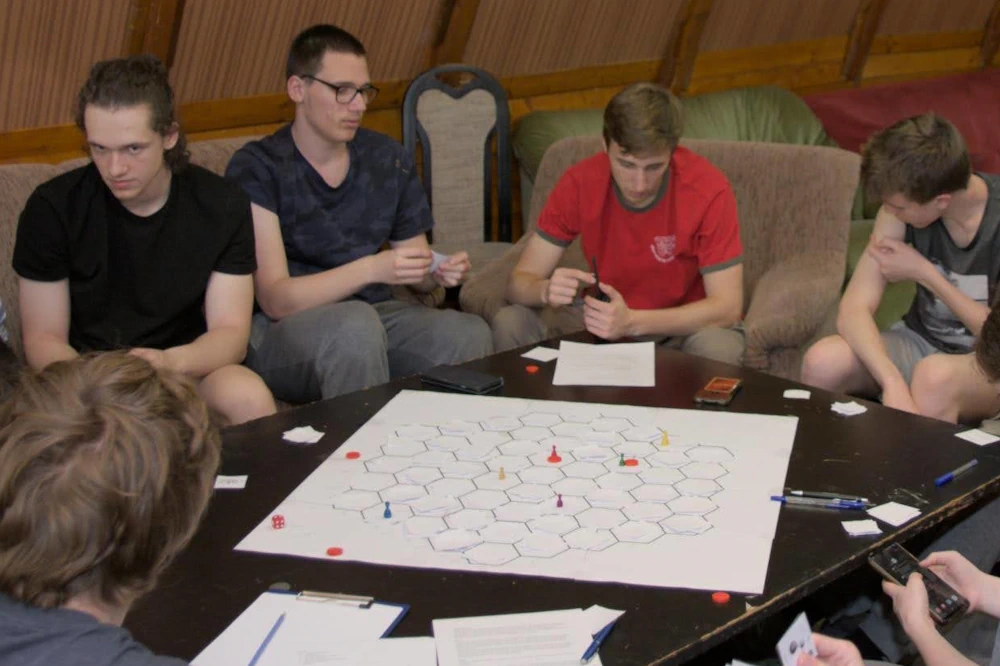 Ǔčastníci sústredenia KSP hrajú plánikovú hru na šesťuholníkovej sieti